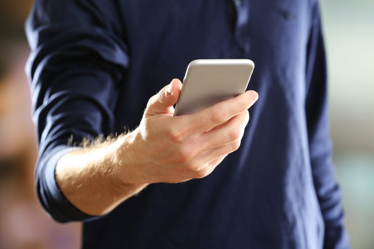 Jak sprawdzić stan konta - grafika do tekstu. Mężczyzna w granatowej koszuli trzymający smartfona w dłoni.