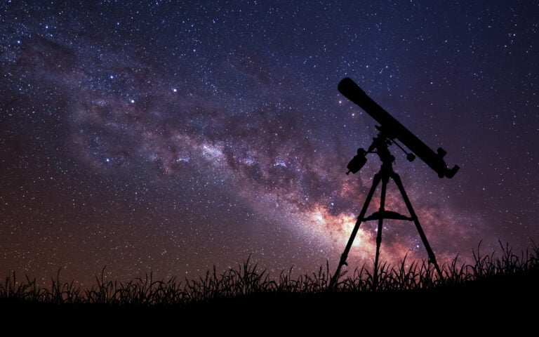 Teleskop astronomiczny na statywie zarysowany na tle gwiaździstego nieba i Drogi Mlecznej.