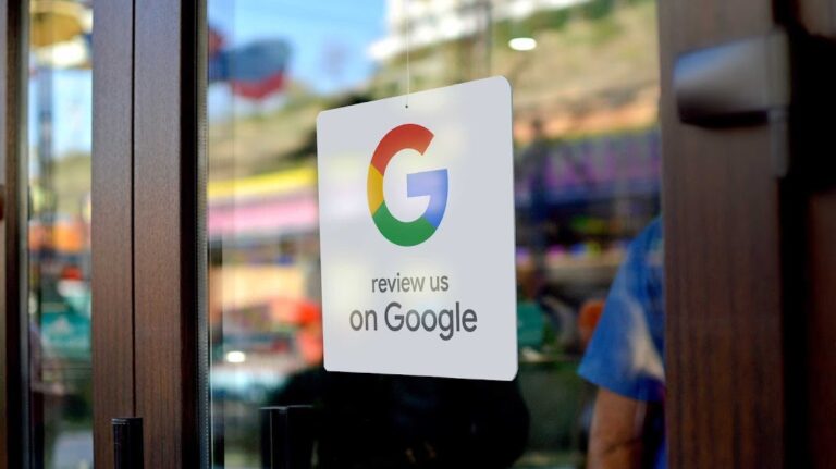 Zawieszka z logo Google i napisem "review us on Google" na drzwiach sklepu z rozmytym tłem przedstawiającym miejsce publiczne.