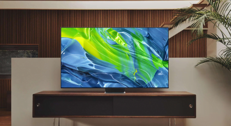 Obraz przedstawia współczesny telewizor na drewnianej szafce przeciwko ścianie z drewnianą okładziną. Na ekranie telewizora widać abstrakcyjną grafikę w odcieniach niebieskiego i zielonego. Obok telewizora stoi doniczka z rośliną o długich liściach.
