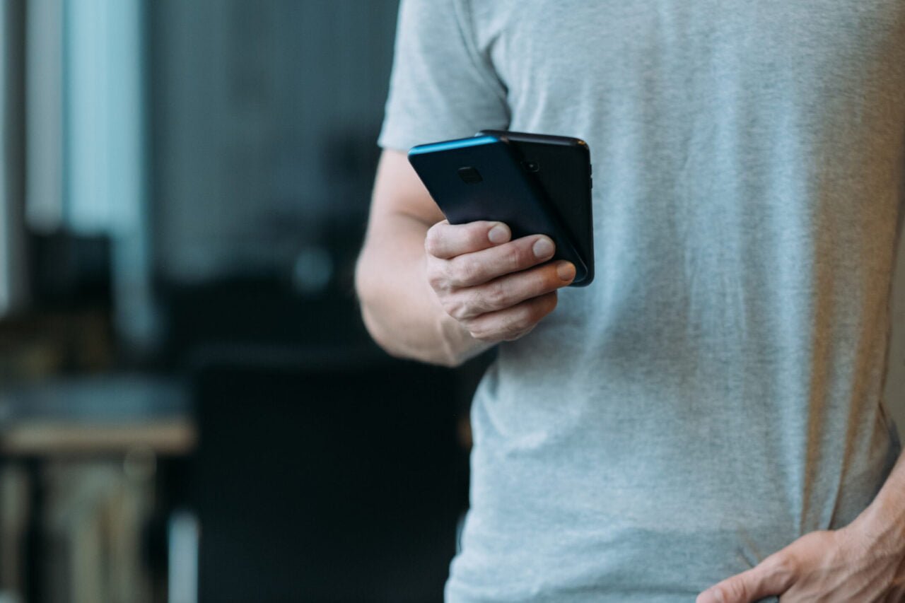 mężczyzna w szarej koszulce trzymający dwa smartfony