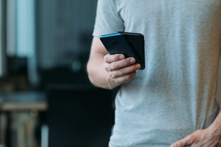 mężczyzna w szarej koszulce trzymający smartfona
