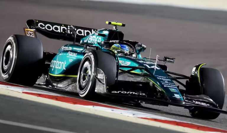 Samochód F1 w kolorach czarno-zielonych, jadący z dużą prędkością na torze wyścigowym, z widocznymi odblaskowymi pasami przy krawędziach toru.