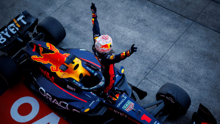 Kierowca wyścigowy świętujący zwycięstwo, stojąc na swoim bolidzie Formuły 1 z uniesionymi w górę rękami.