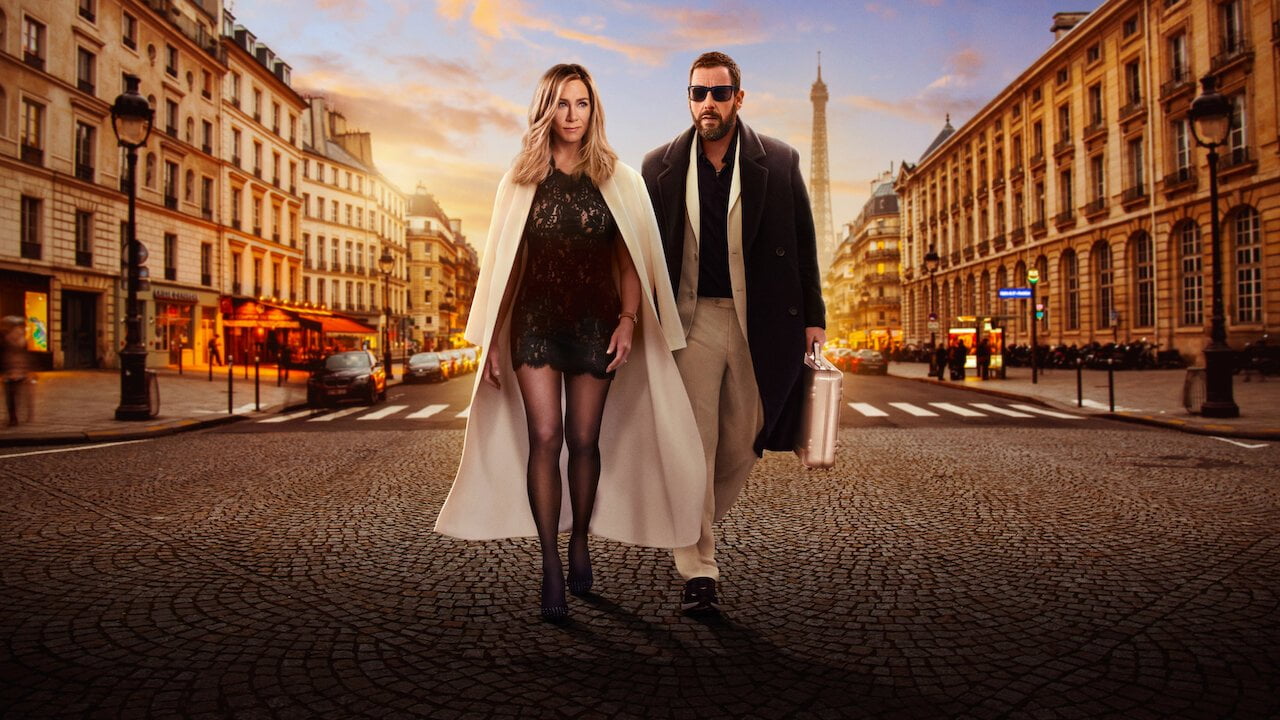 Jennifer Aniston oraz Adam Sandler idący po brukowanej drodze. Po obu stronach widoczne zabytkowe budynki Paryża