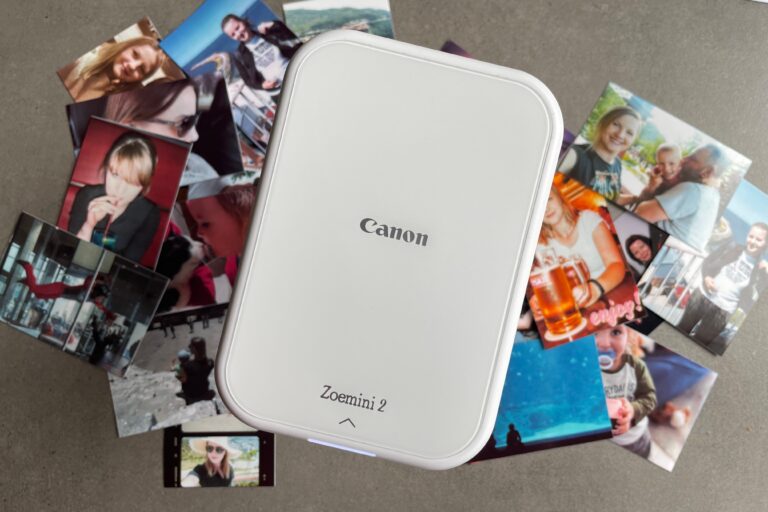 Biała przenośna drukarka fotograficzna Canon Zoemini 2 otoczona różnymi wydrukowanymi zdjęciami.