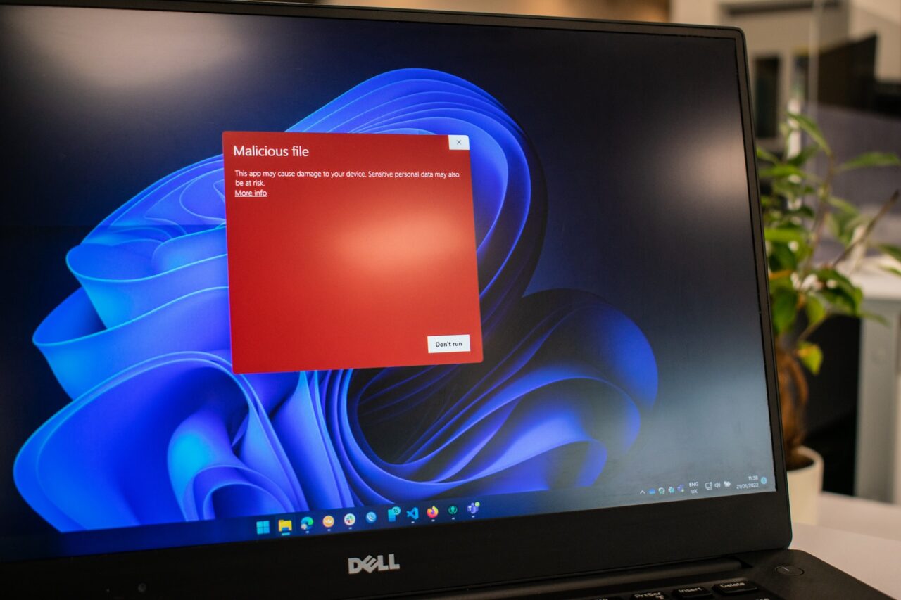 Monitor komputera z ostrzeżeniem o szkodliwym pliku wykrytym przez Microsoft Defender na ekranie, z widocznymi ikonami aplikacji na pasku zadań.