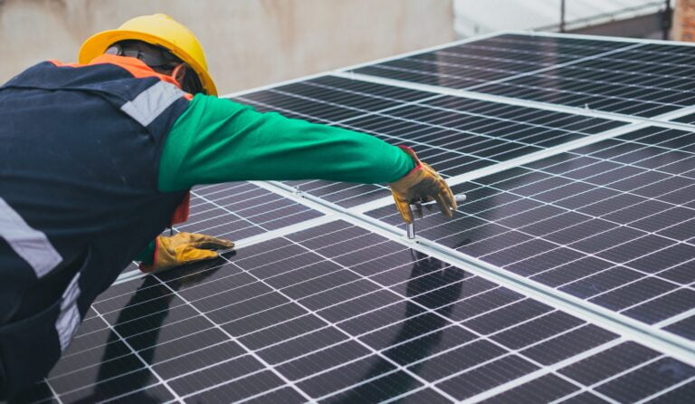 Pracownik w kasku ochronnym montuje panele słoneczne na metalowej konstrukcji. Fotowoltaika w 2024 roku będzie bardzo popularna