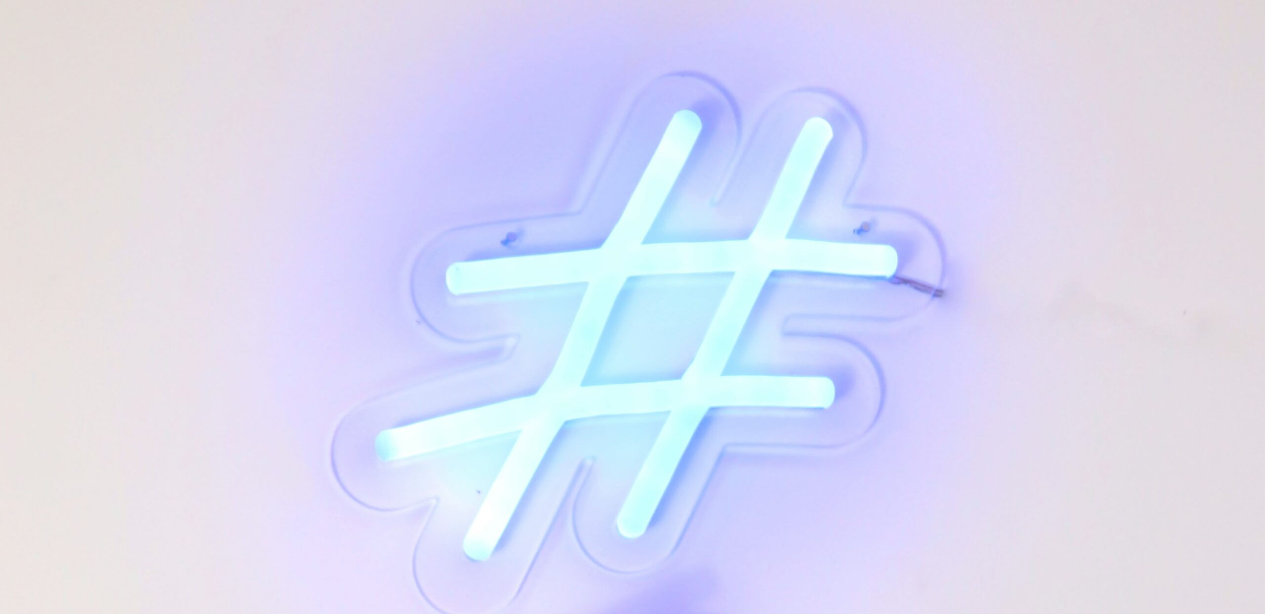 Świecący neon w kształcie znaku hashtag na rozmytym białym tle.