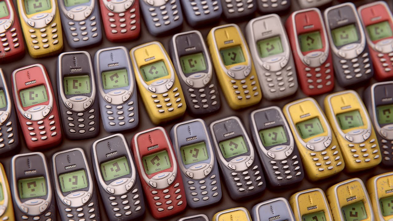Zbiór klasycznych telefonów komórkowych Nokia w różnych kolorach ułożonych obok siebie.