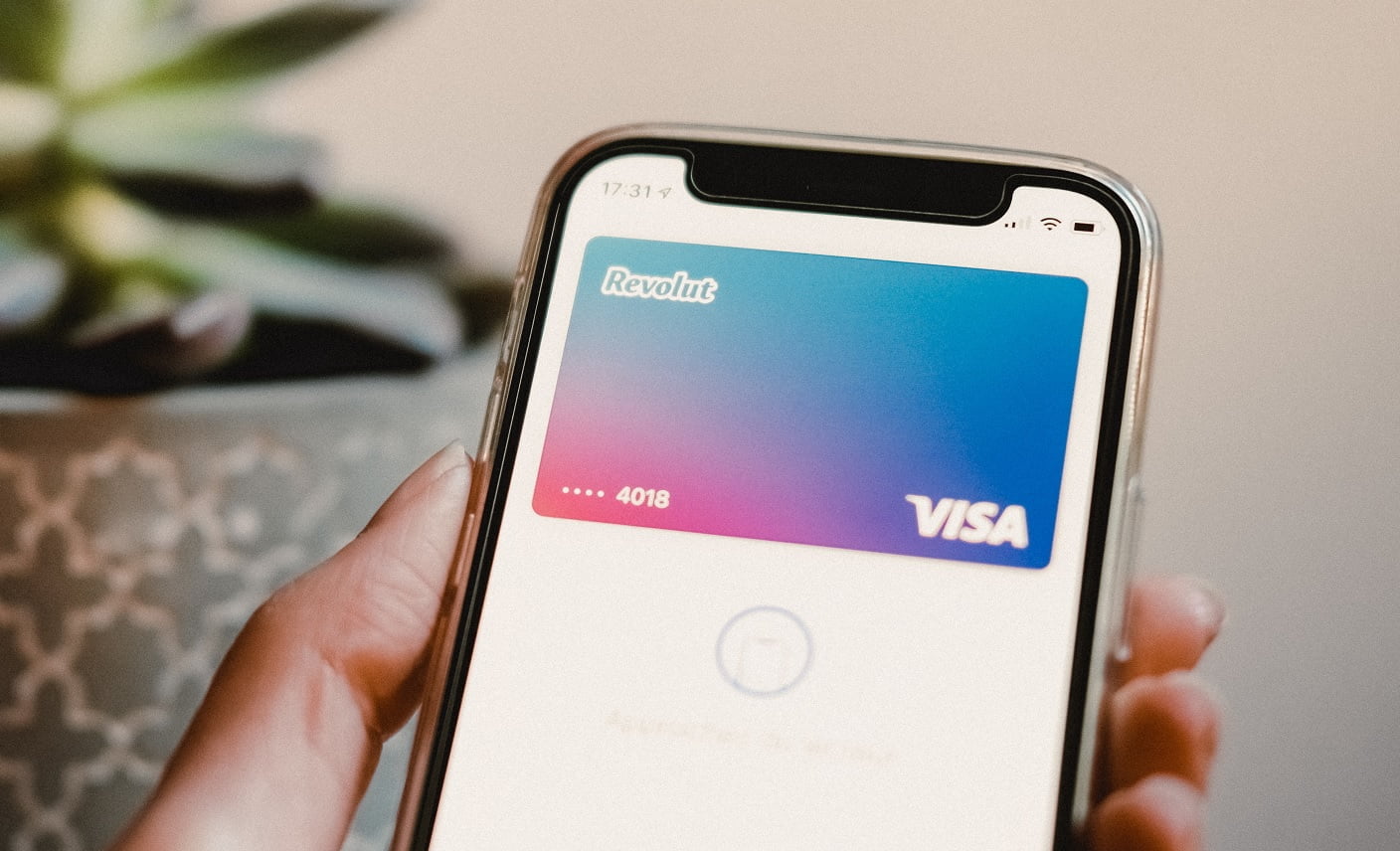 Osoba trzyma smartfon wyświetlający wirtualną kartę płatniczą Revolut Visa na ekranie, z widocznymi ostatnimi cyframi numeru karty i gradientem kolorów w tle.
