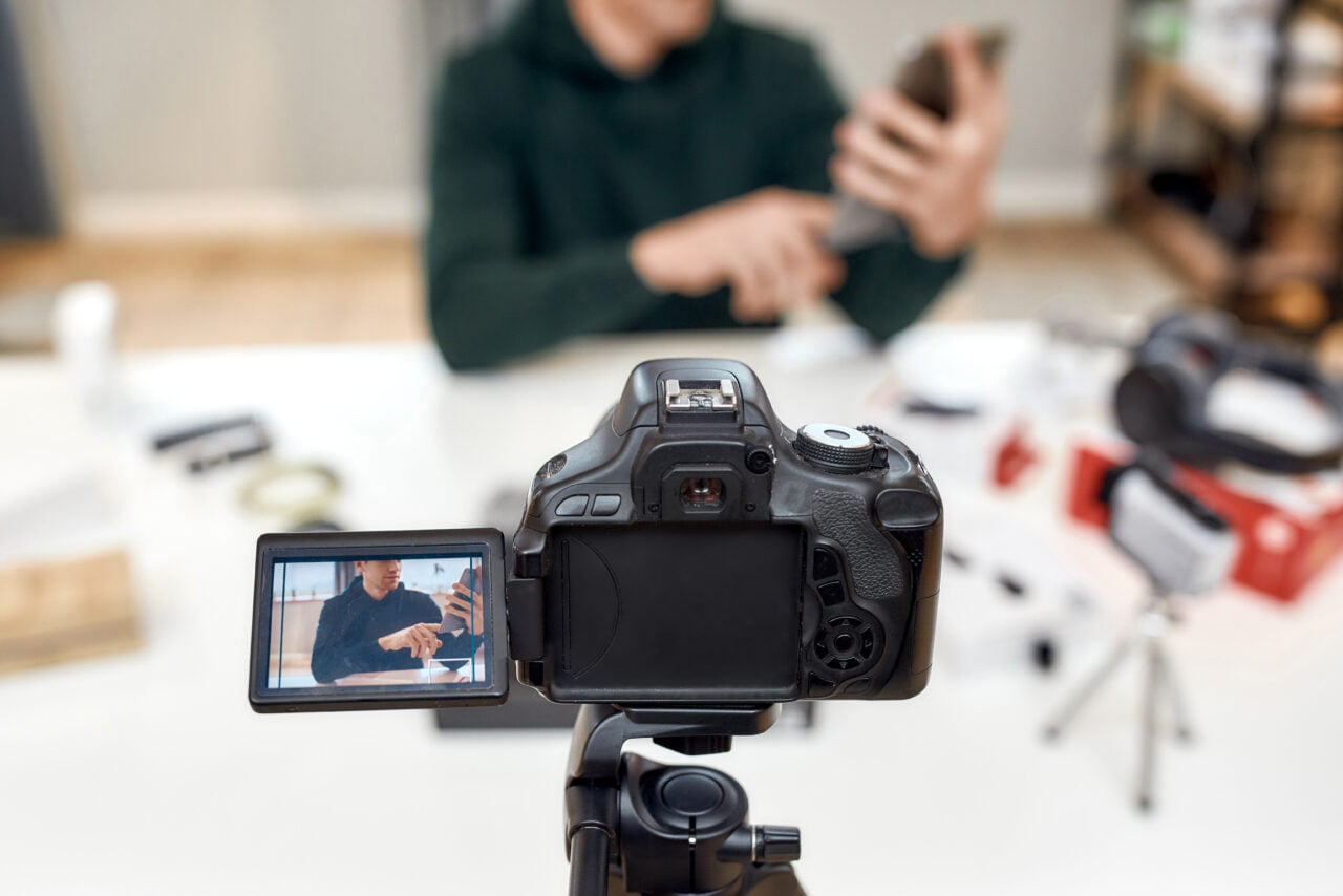 Kamera na statywie nagrywająca osobę obsługującą smartfon na biurku.