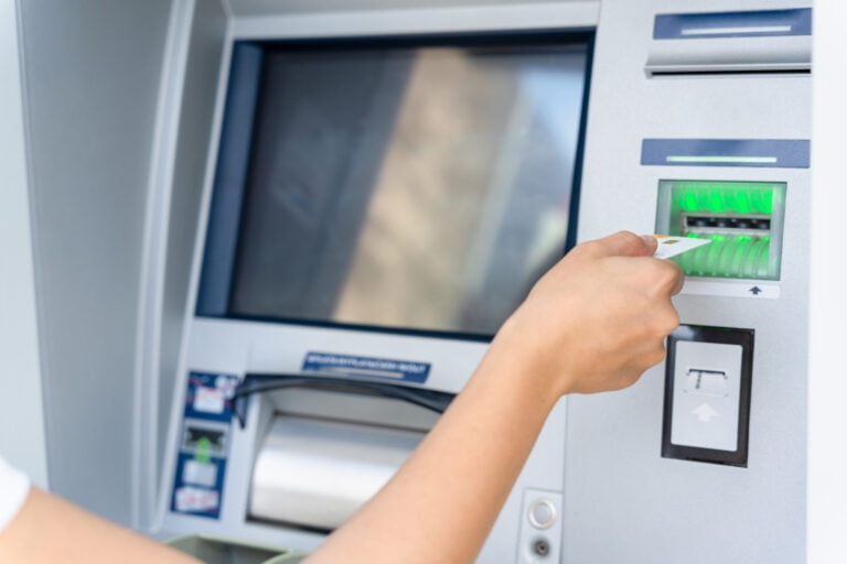 Osoba wkłada kartę bankową do bankomatu.