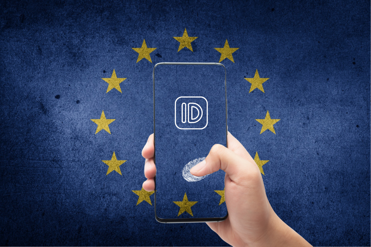 Dłoń trzymająca smartfon z ikoną ID i odciskiem palca na tle flagi Unii Europejskiej.