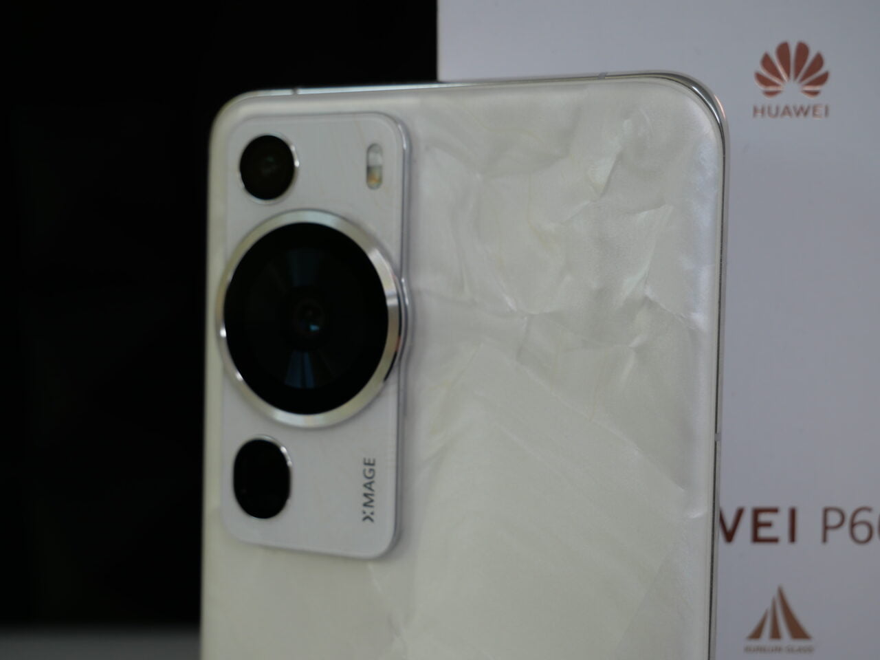 Tylna część smartfona Huawei z widocznym modułem aparatu o podwójnym obiektywie i etykietą XMAGE, umieszczona na tle opakowania z logo Huawei.