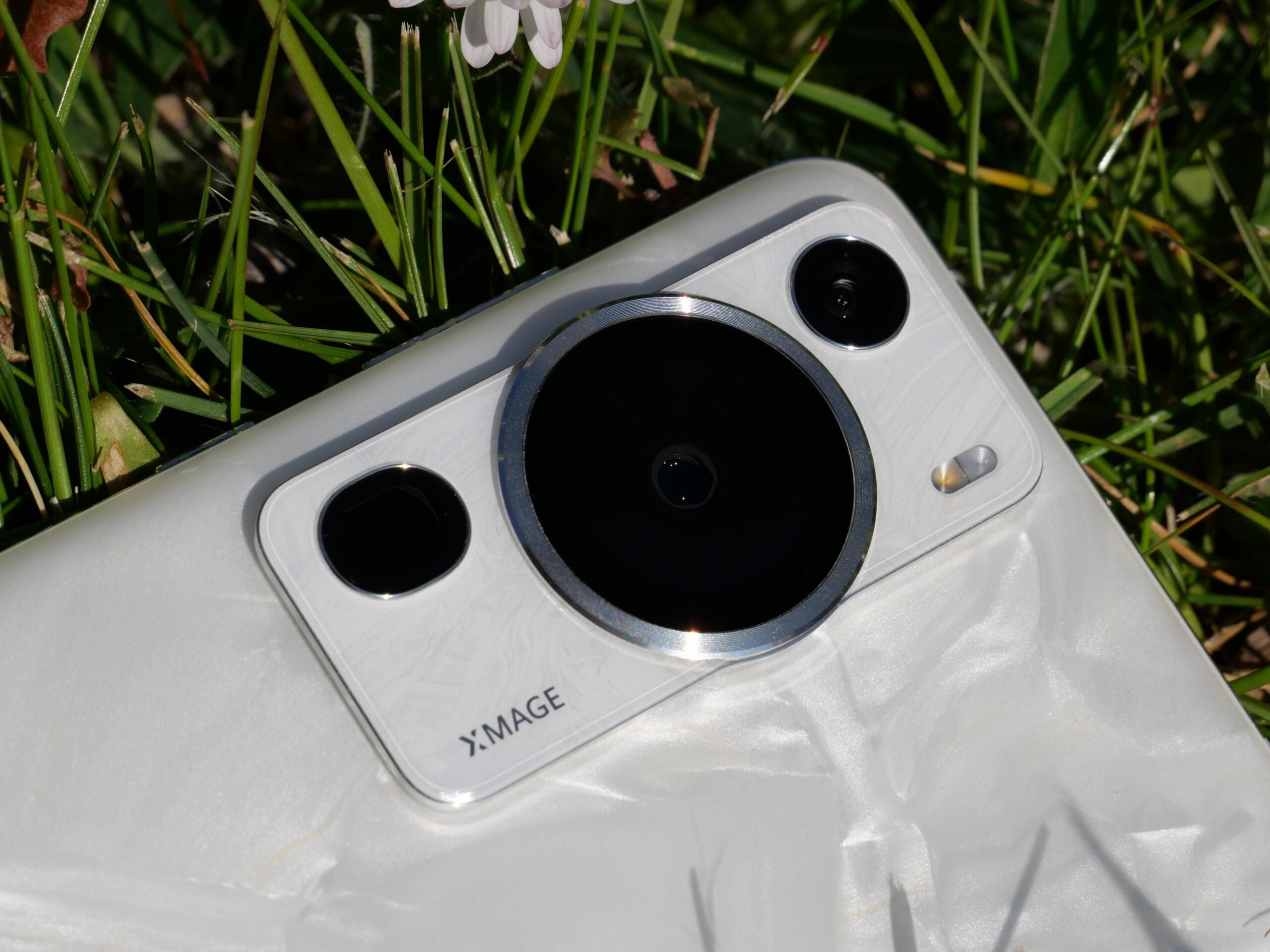 Biały smartfon z potrójnym aparatem leżący na trawie.