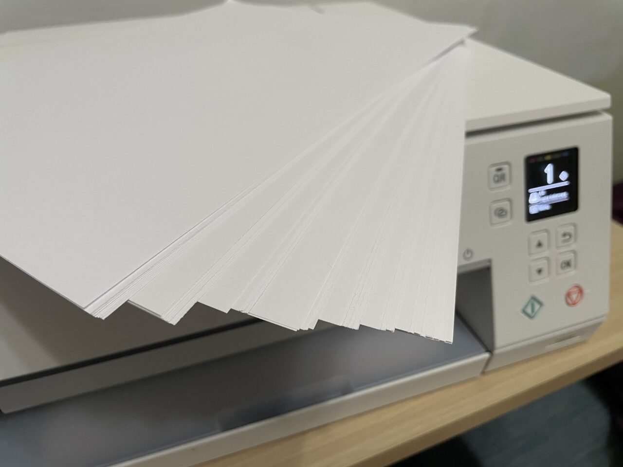 Stos białych kartek papieru na górze białej drukarki z włączonym wyświetlaczem pokazującym numer 1.