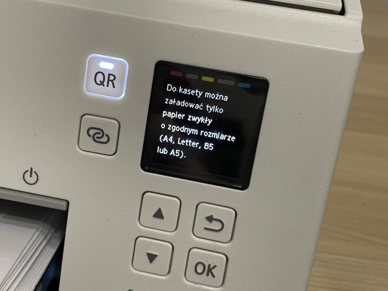 Drukarka nie pobiera papieru. Panel sterowania drukarki z podświetlonym przyciskiem "QR" i wyświetlaczem LCD pokazującym komunikat w języku polskim o załadunku papieru o standardowych rozmiarach.