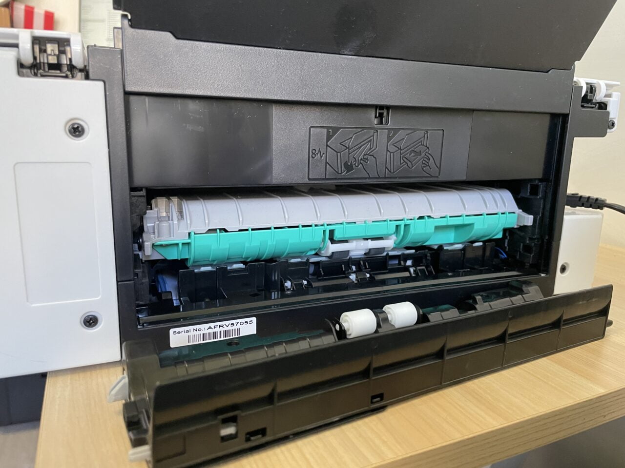 Otwarta drukarka laserowa z widocznym wkładem z tonerem i instrukcjami wymiany wkładu na klapie.