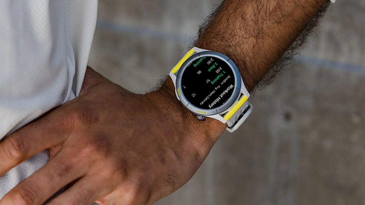 Zdjęcie zbliżenia męskiego nadgarstka z noszonym na nim inteligentnym zegarkiem z białym paskiem i żółto-czarnymi akcentami na tarczy wyświetlającej dane o kondycji.