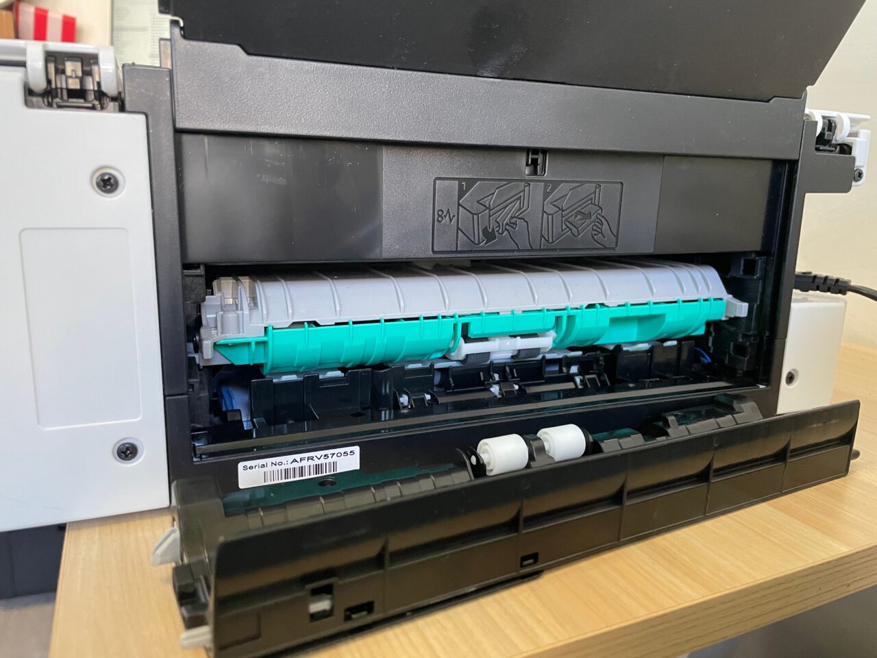 Wnętrze otwartej drukarki laserowej z widocznym bębnem i tonerem na biurku.