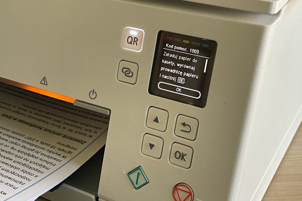 Panel sterowania drukarki z wyświetlaczem LCD pokazującym komunikat o błędzie oraz klawiszami nawigacyjnymi i przyciskiem QR.