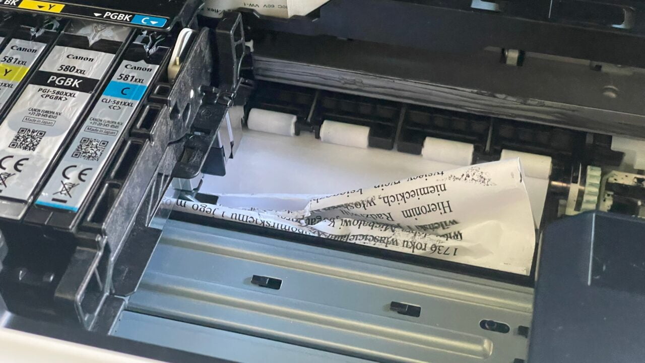 Zacięty arkusz papieru w drukarce atramentowej z widocznymi kartridżami tuszu.