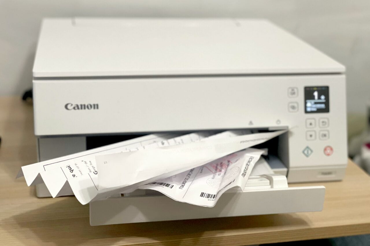 Biała drukarka Canon z wydrukowanymi dokumentami leżącymi w zagłębieniu na wydruki.