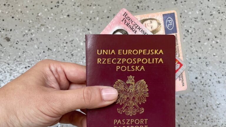 Dłoń trzymająca czerwony polski paszport z napisem "UNIA EUROPEJSKA RZECZPOSPOLITA POLSKA PASZPORT" oraz częściowo widoczny polski dowód osobisty.