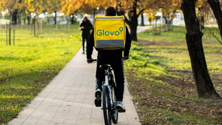 Kurier Glovo na rowerze jedzie ścieżką w parku.