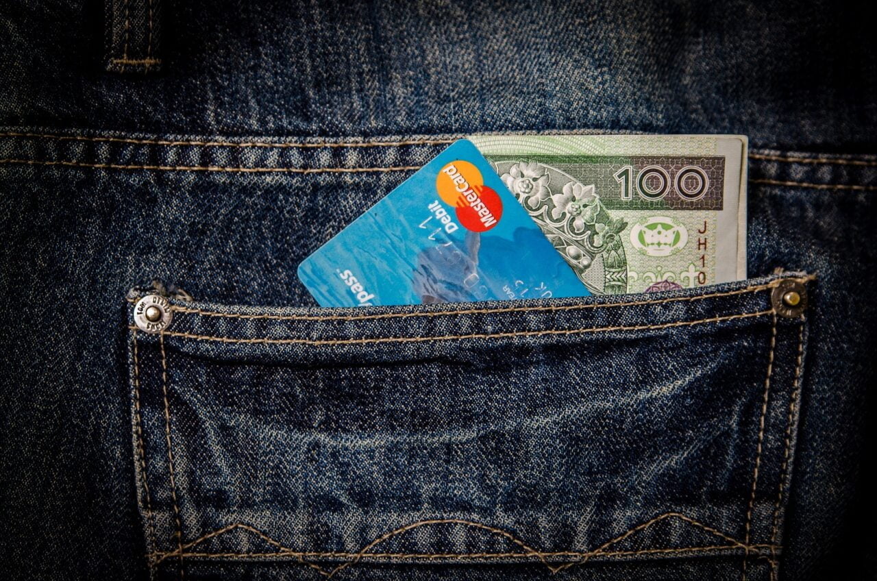 Niebieskie dżinsowe spodnie z banknotem o nominale stu złotych i niebieską kartą kredytową Mastercard wystającymi z tylnej kieszeni.