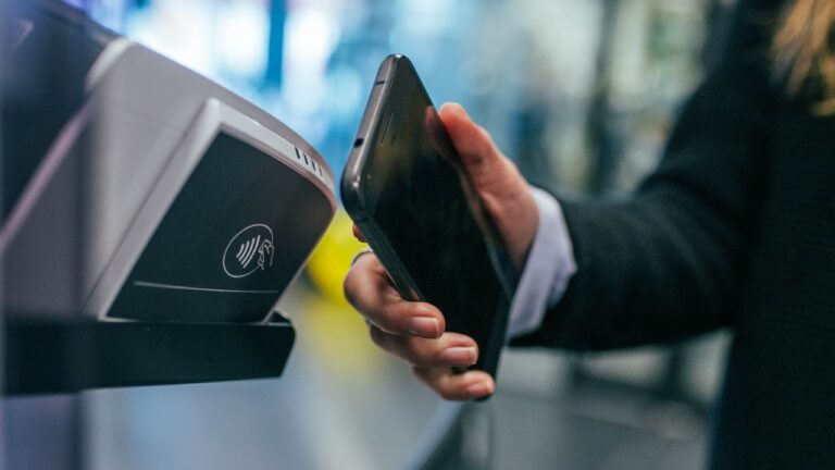 Osoba dokonuje płatności zbliżeniowej smartfonem przy terminalu płatniczym.