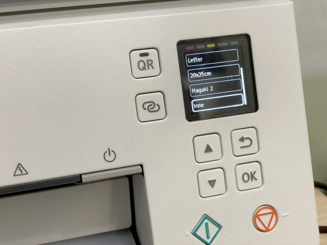 Panel sterowania drukarki z ekranem dotykowym wyświetlającym opcje formatów papieru i przyciski nawigacyjne.