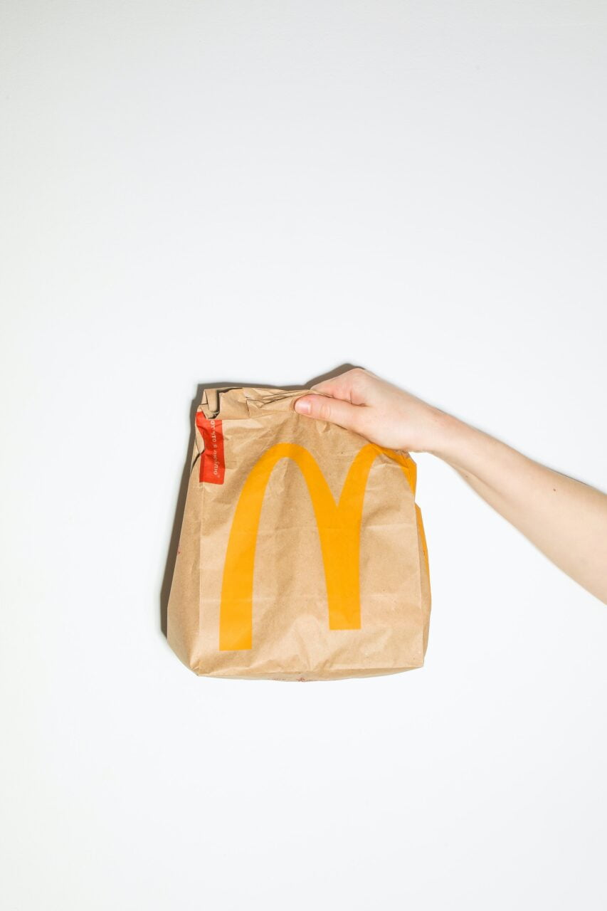Torba z logo McDonald's trzymana przez dłoń na białym tle.