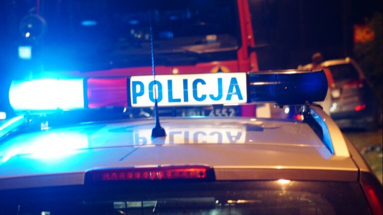 Radiowóz policji z włączonymi niebieskimi światłami alarmowymi w nocy.