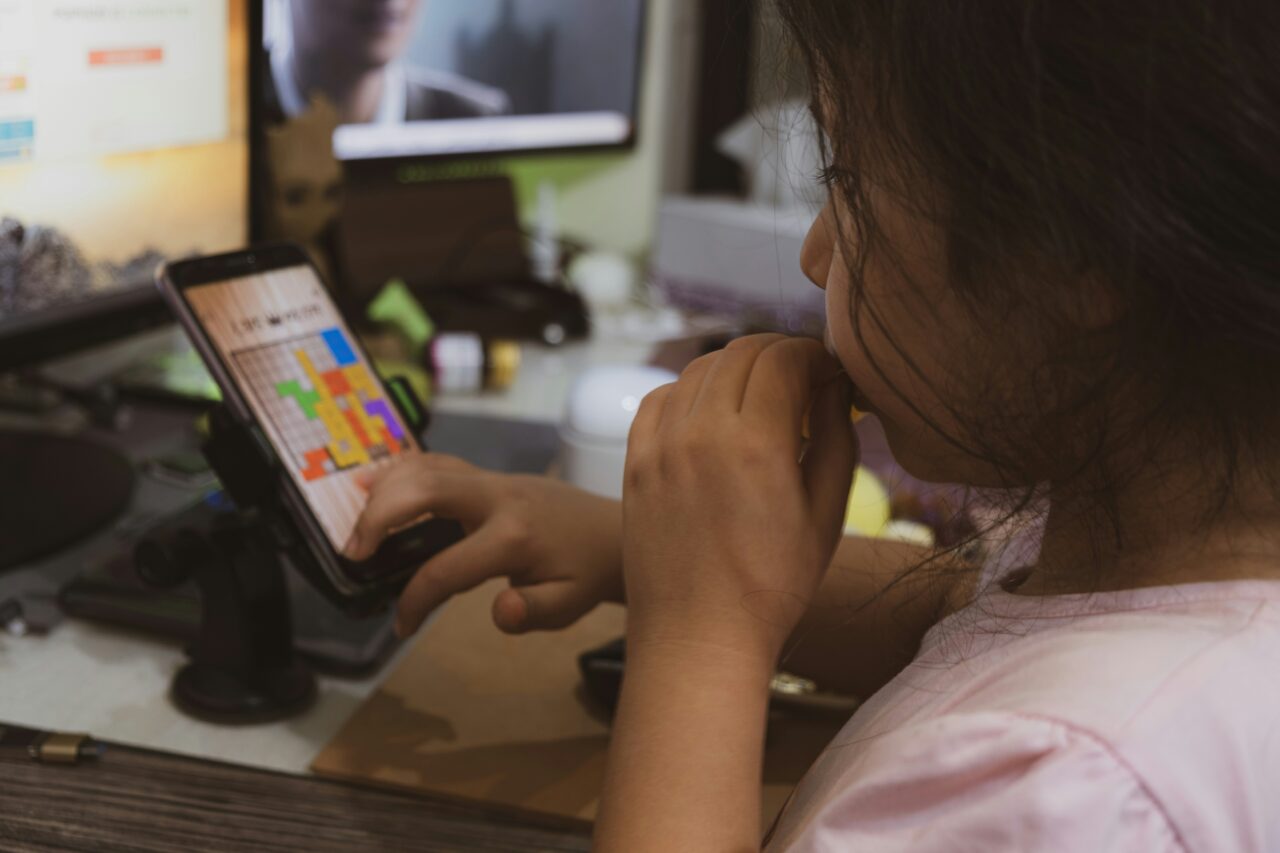 Dziewczyna grająca w kolorową grę logiczną na smartfonie zamocowanym na statywie na biurku.