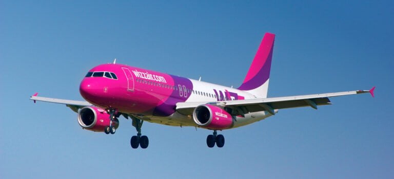 Samolot pasażerski o barwie różowej na tle błękitnego nieba w trakcie lądowania.
