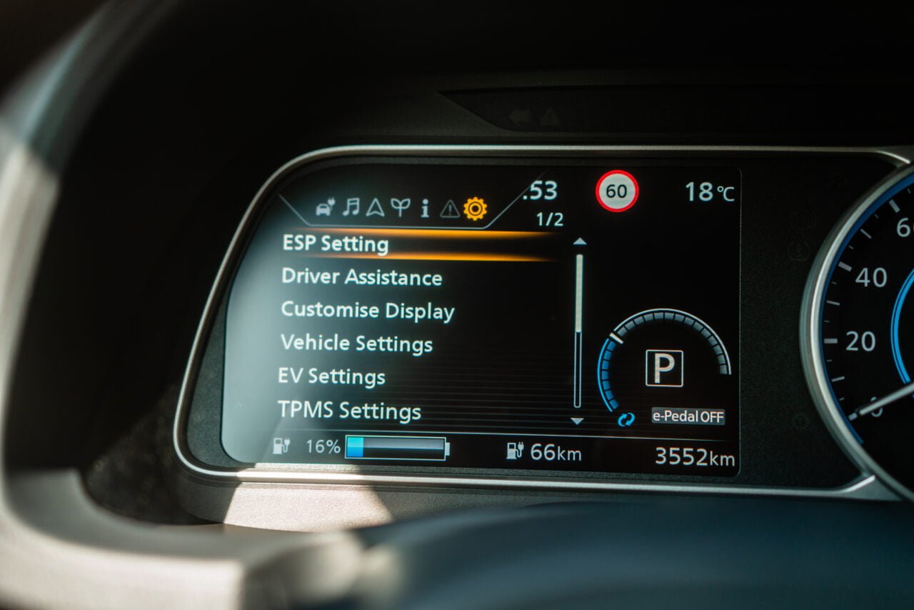 Cyfrowy wyświetlacz deski rozdzielczej samochodu pokazujący menu ustawień pojazdu, wskaźnik baterii z 16% naładowania, zasięg 66 km i przebieg 3552 km oraz temperaturę zewnętrzną 18°C.