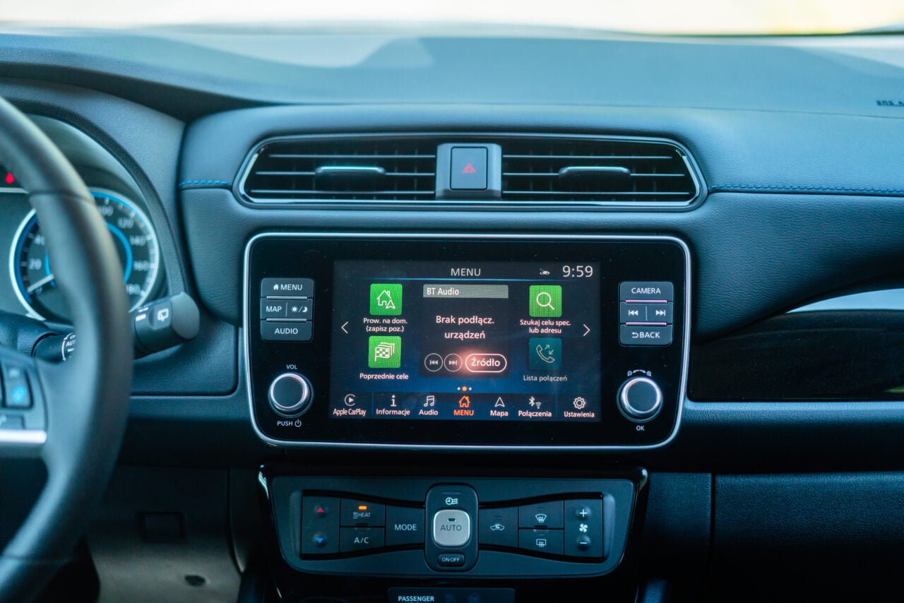 Wnętrze samochodu z widokiem na kierownicę i centralną konsolę z ekranem dotykowym wyświetlającym menu systemu multimedialnego w języku polskim.