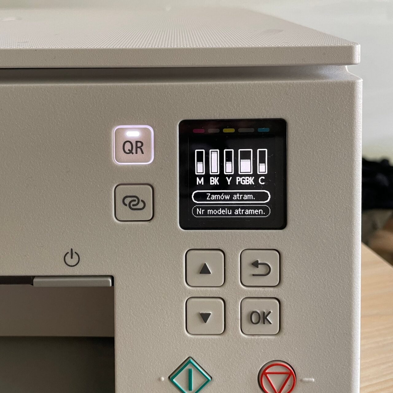 Panel sterowania drukarki z ekranem pokazującym poziomy atramentu i przyciskami, w tym przycisk z kodem QR i ekran z wyświetlaczem stanu tuszy.