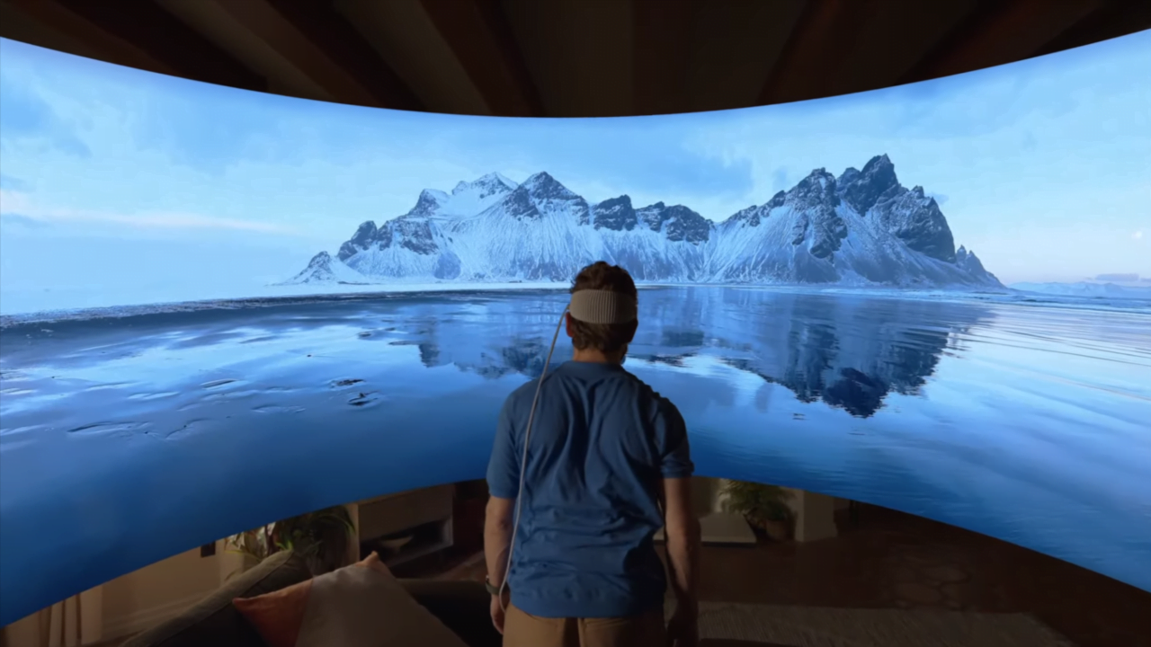 Osoba w pomieszczeniu z zakrzywionym ekranem wyświetlającym wirtualny krajobraz górski odbijający się w jeziorze.