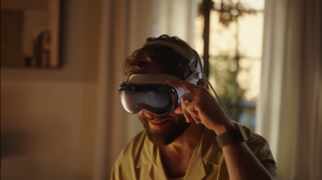 Mężczyzna w koszuli z krótkim rękawem używa gogli wirtualnej rzeczywistości Apple Vision Pro w jasnym pomieszczeniu.