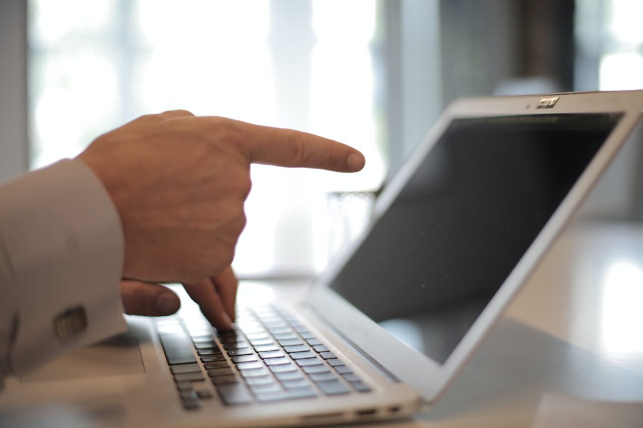 Męska dłoń wskazująca palcem na wyłączony ekran laptopa.