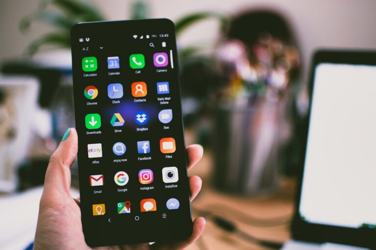 Dłoń trzymająca smartfon z ekranem głównym wyświetlającym różne kolorowe ikony aplikacji.