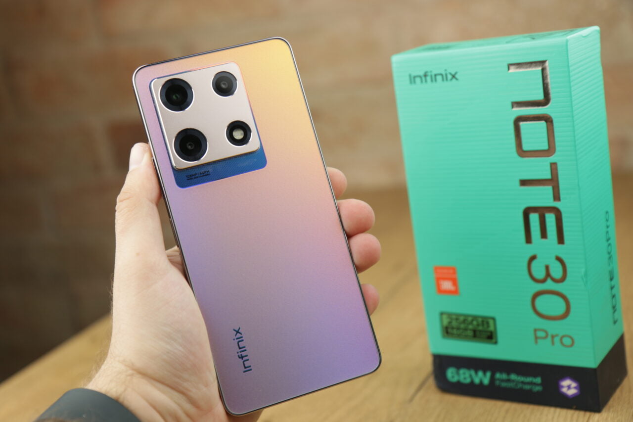 Tylna strona smartfona marki Infinix z gradientowym wykończeniem i potrójnym aparatem fotograficznym, trzymany w dłoni obok zielonego pudełka z napisem "Infinix NOTE 30 Pro".