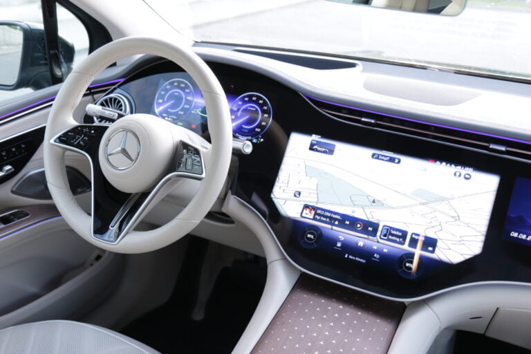 Wnętrze samochodu Mercedes-Benz z widoczną kierownicą i deska rozdzielczą z cyfrowymi wyświetlaczami, w tym dużym ekranem nawigacji GPS.