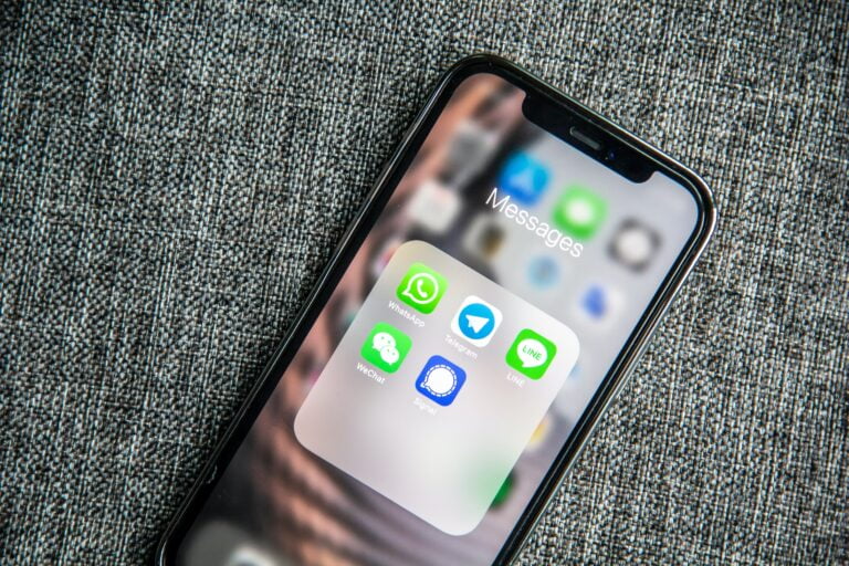 Smartfon leżący na szarej tkaninie, z wyświetlaczem pokazującym folder aplikacji komunikacyjnych takich jak WhatsApp, Telegram, WeChat i Signal.