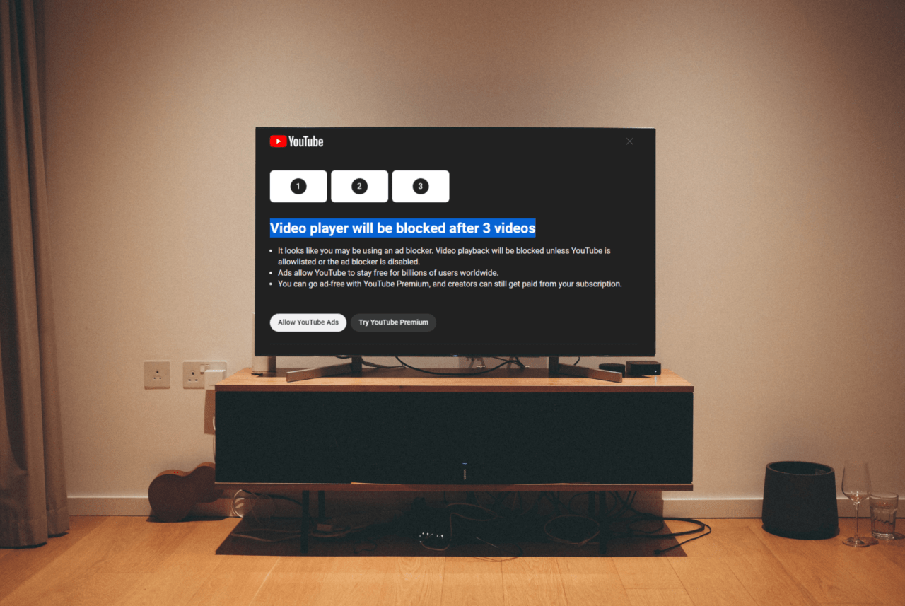 Reklamy na YouTube i sposób blokady. Telewizor w salonie wyświetla komunikat YouTube informujący o zablokowaniu odtwarzacza wideo po 3 filmach w przypadku wykrycia blokowania reklam.