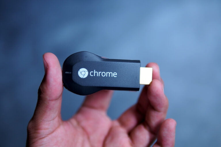 Urządzenie Google Chromecast trzymane w dłoni na niebieskim tle.