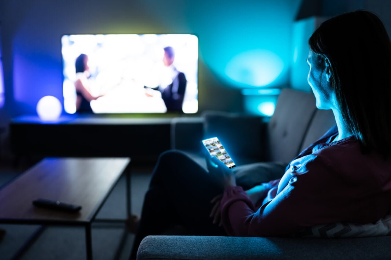 Kobieta oglądająca telewizję w ciemnym pokoju, trzyma pilota do telewizora. Streaming pokonał dawne sposoby przesyłania danych, np. sieci P2P i BitTorrent